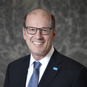Jonathon Reckford, a middle-aged white man, balding, with dark hair and glasses, dressed in a dark blue suit, white shirt, blue tie