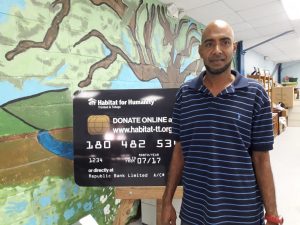 Advocacy Build Homeowner Andy, stands in front of a giant credit card promoting Habitat's online donation facility at habitat-tt.org/donate-now